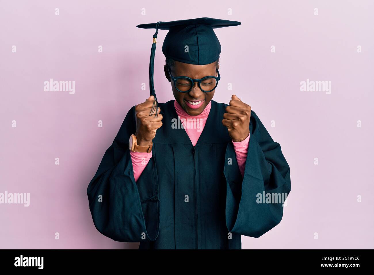 Young african american girl wearing graduation cap and ceremony robe excited for success with arms raised and eyes closed celebrating victory smiling. Stock Photo