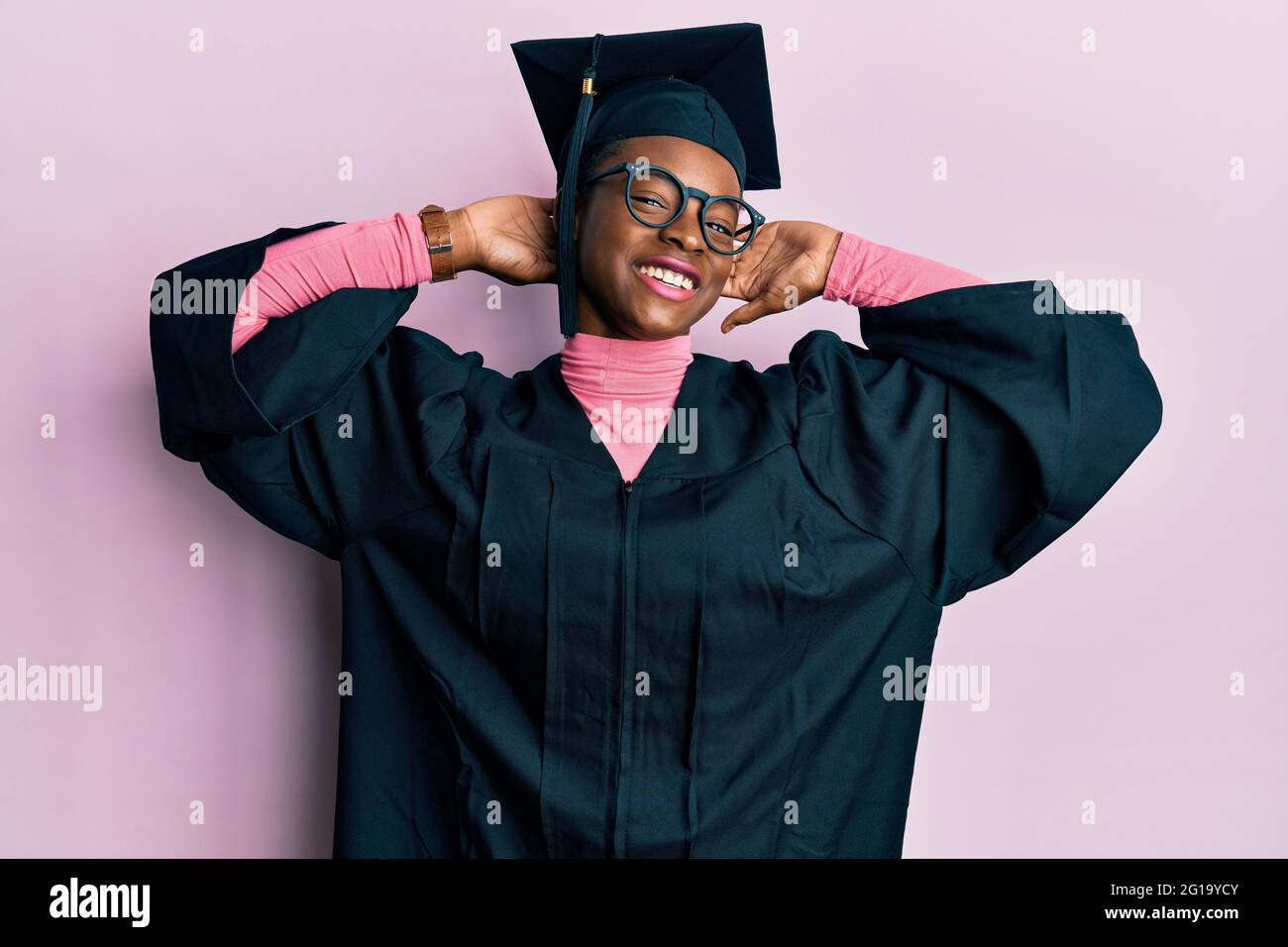 Young african american girl wearing graduation cap and ceremony robe relaxing and stretching, arms and hands behind head and neck smiling happy Stock Photo