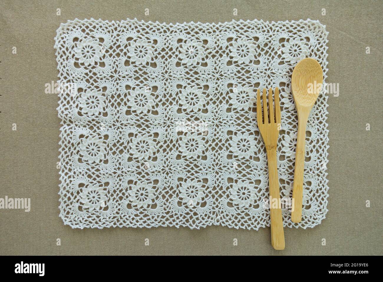Wooden utensils, bamboo spoon and fork on a white handcraft crochet place mat. Minimal eco friendly home style uses as background and copy space. Stock Photo