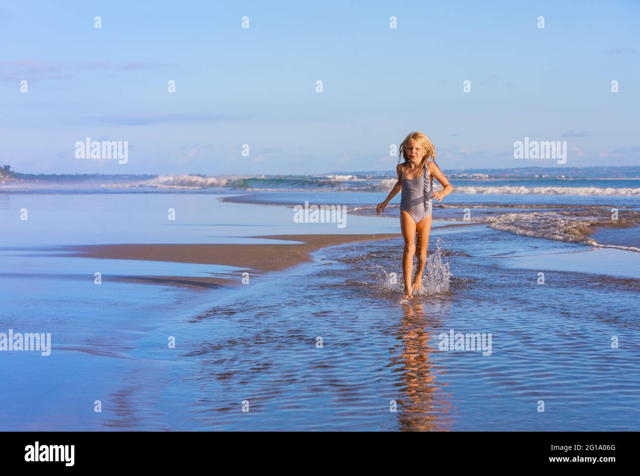 Young happy girl have fun, run by water pool along sea surf and jump on sand beach. Popular travel destination. Family summer vacation with kids Stock Photo