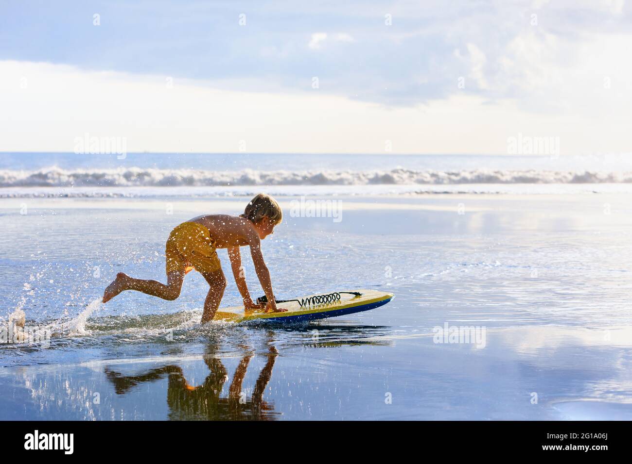 Happy boy - young surfer with bodyboard have fun on beach, run by sea water pool. Active family lifestyle, kids outdoor water sport, swimming activity Stock Photo
