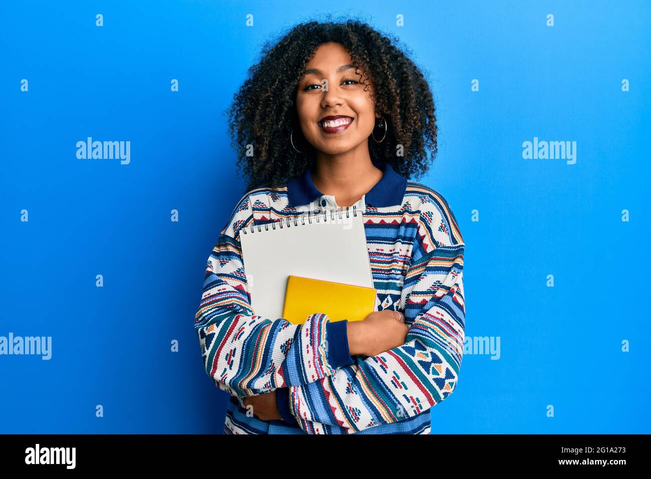 Beautiful african american woman with afro hair holding books smiling ...