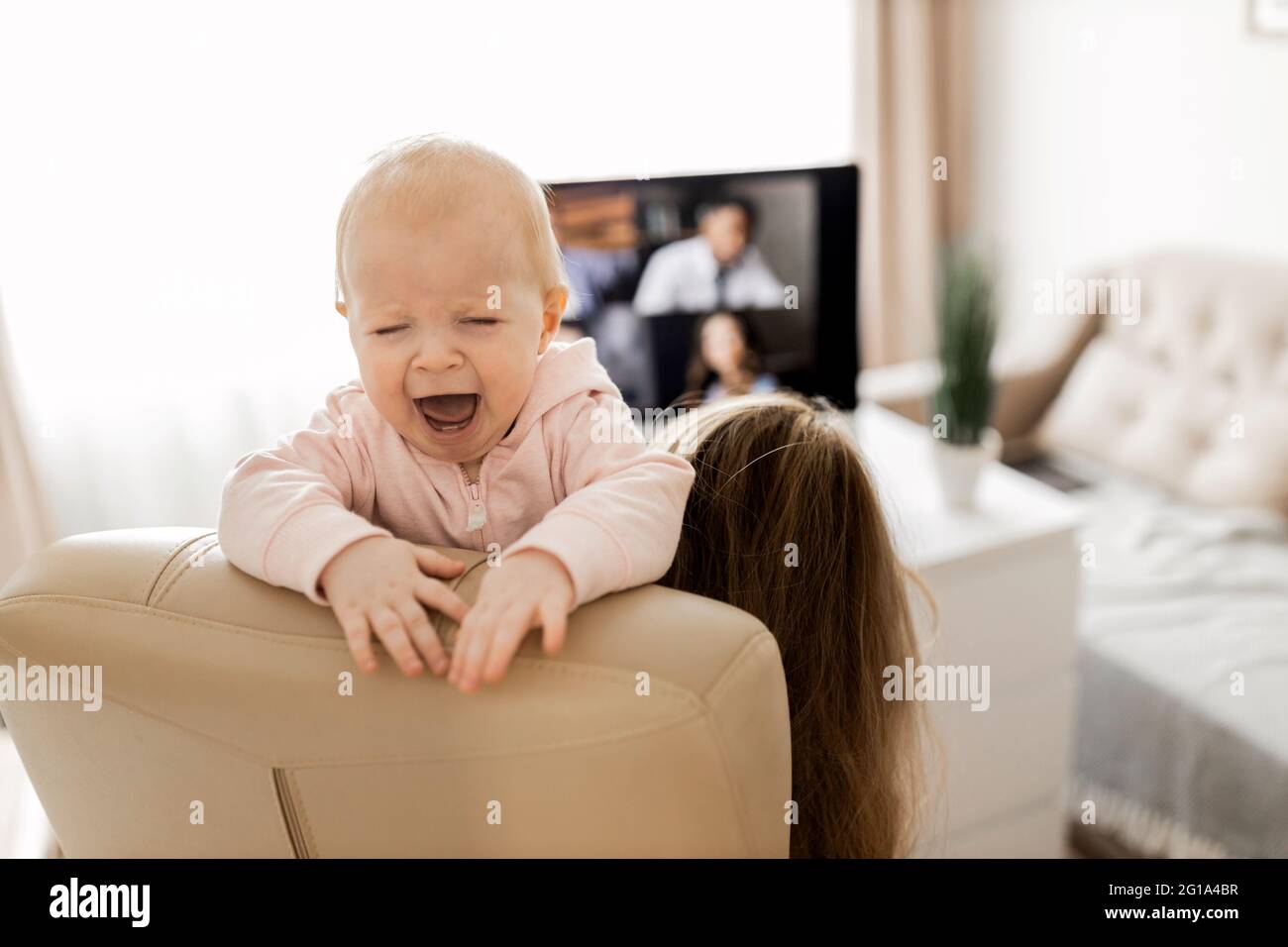 Young woman working at desk at home with computer holding crying tired infant baby holding business meeting at home, online pediatric consultation Stock Photo