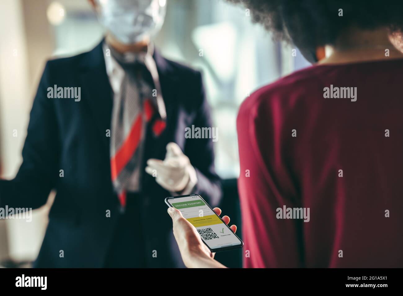 Female traveler holding mobile phone with vaccine passport at airport check-in counter. Woman passenger checking in at airport with her immunity passp Stock Photo