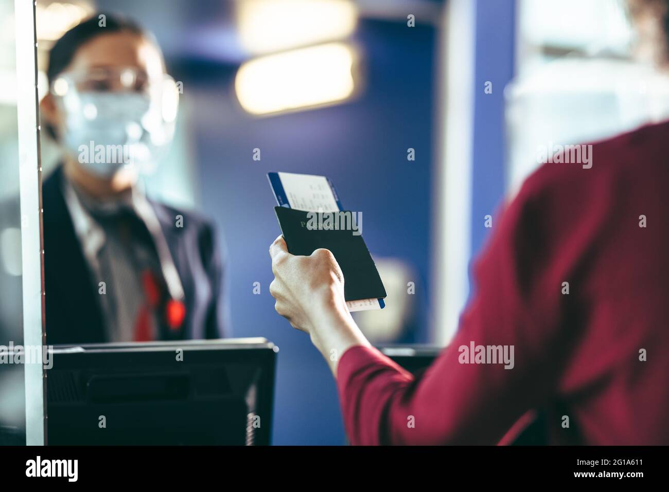 Cropped shot of a female passenger giving her passport with flight ticket to airline attendant behind check-in counter during covid-19 outbreak. Woman Stock Photo