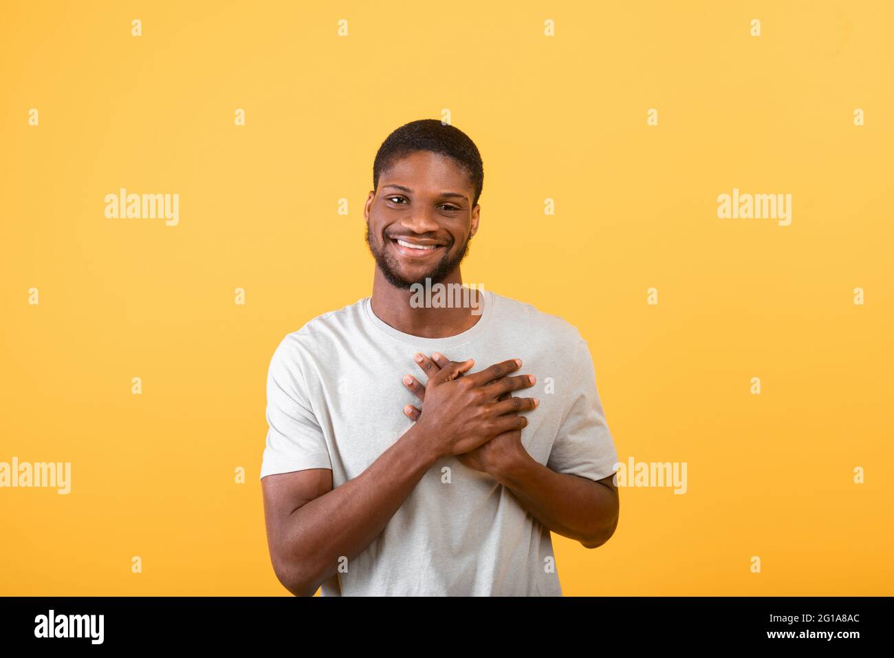 Pleased guy keeping palms on heart, feeling hope and love over yellow background, studio shot Stock Photo