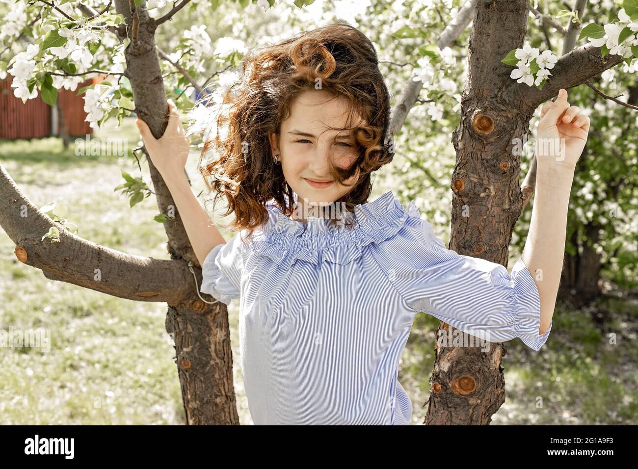 Lifestyle photo. Cute pretty smiling young brunette girl in a blooming garden. Spring photo shot against the background of blooming apple trees. Happy Stock Photo