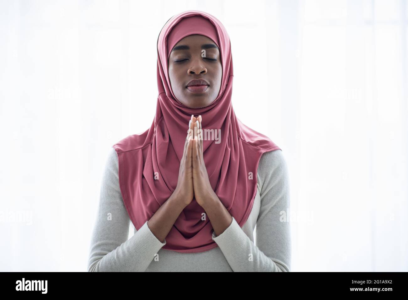 Portrait Of Black Muslim Lady Praying With Clasped Hands And Closed Eyes Stock Photo