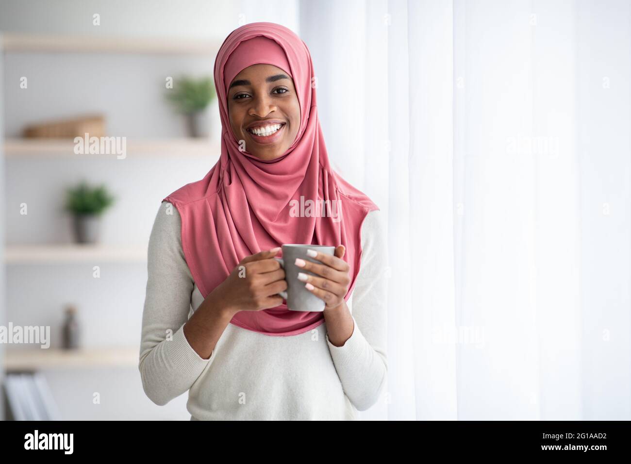 Happy Black Muslim Woman In Hijab Drinking Coffee Near Window At Home ...