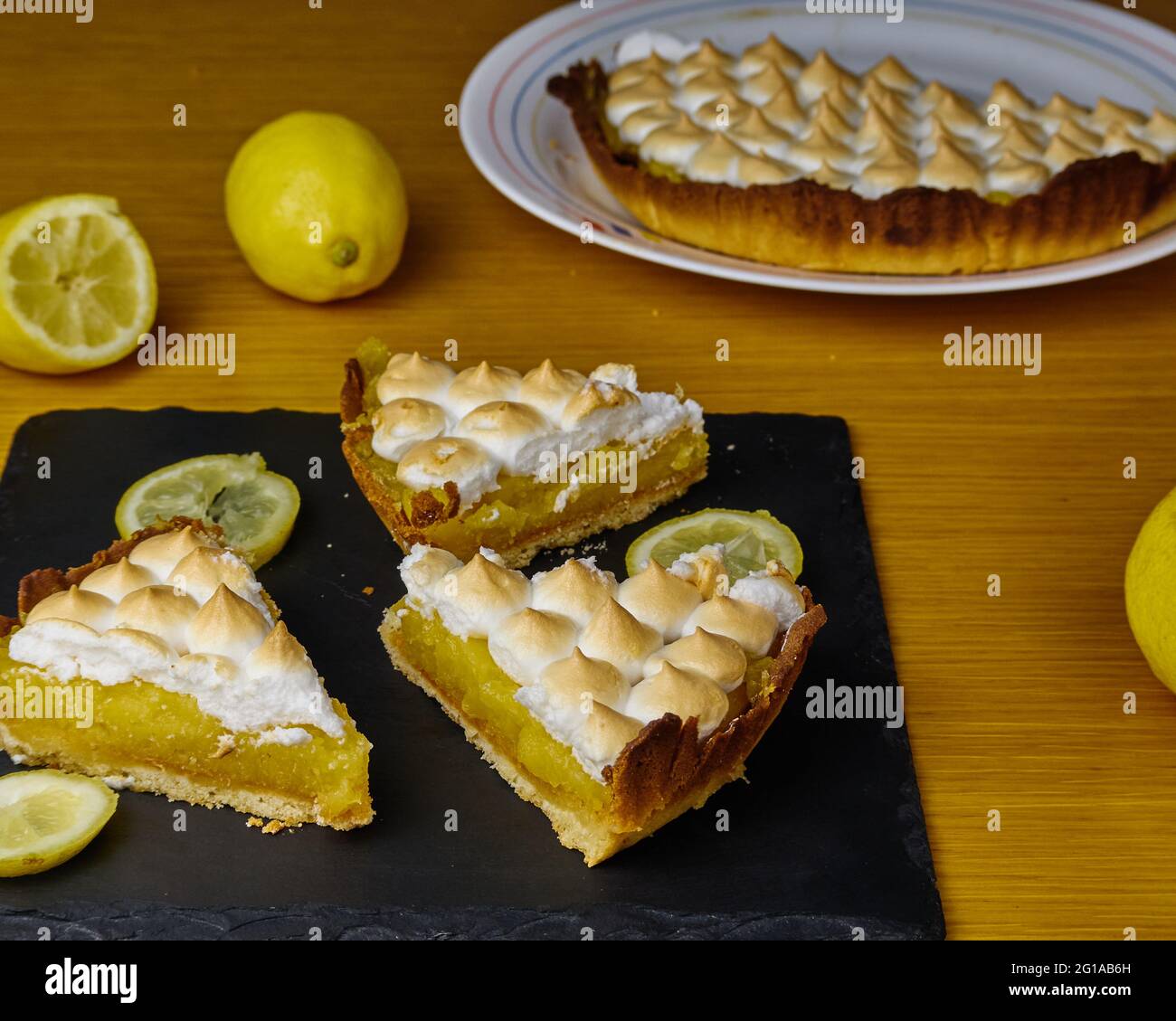 Three Lemon Pie slices on a black slate board decorated with lemons and the rest of the cake Stock Photo