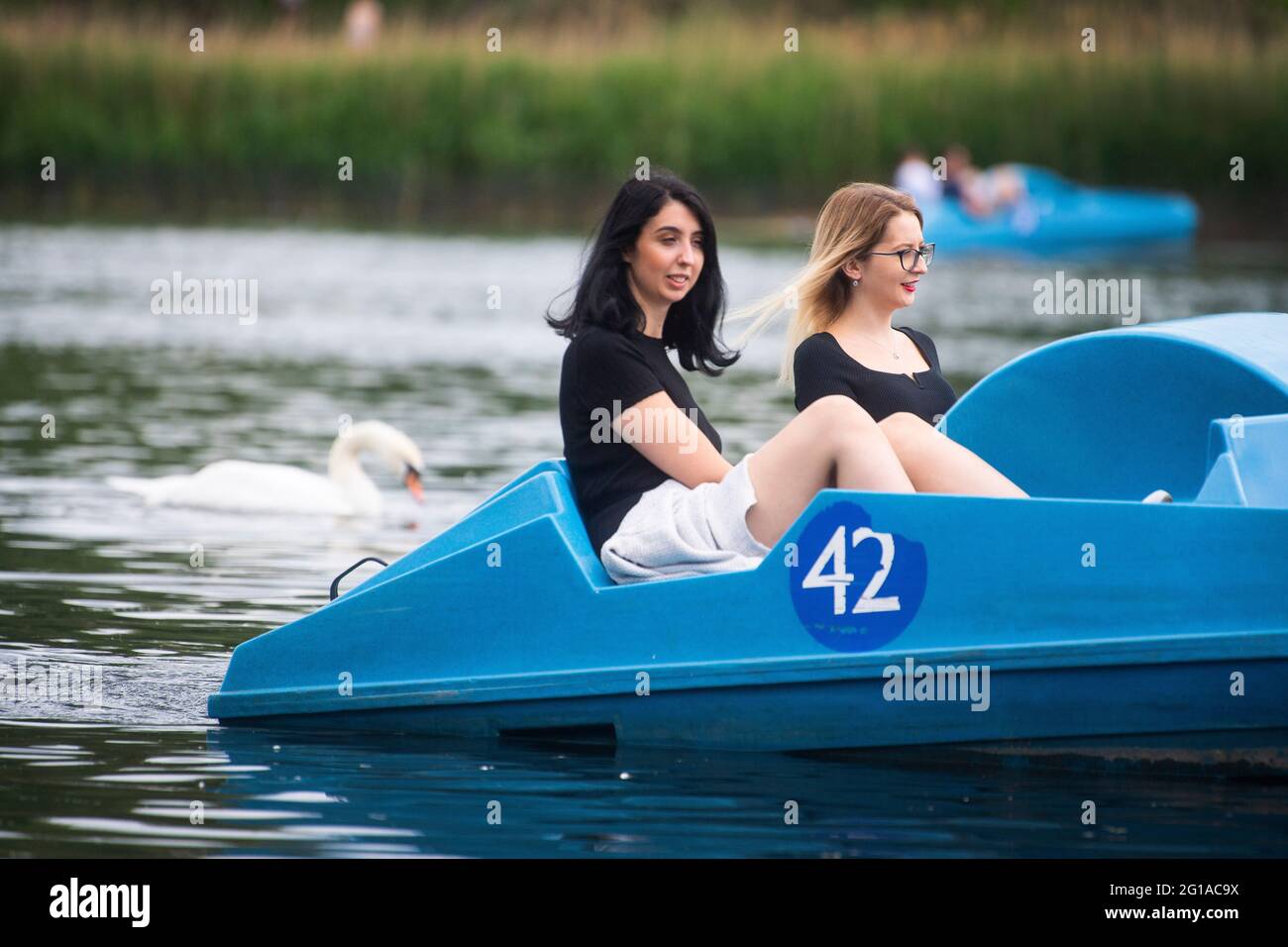 Two women ride a pedalo boat on the Serpentine in Hyde Park, London, as