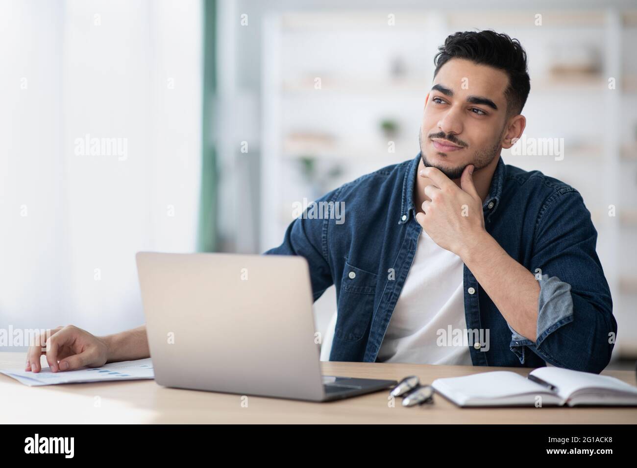 Dreamy young man sitting at office, looking at copy space Stock Photo