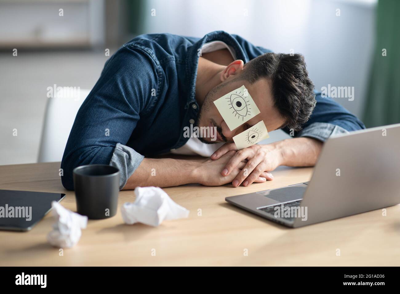 Exhausted arab guy with eyes drawing sleeping at workdesk Stock Photo