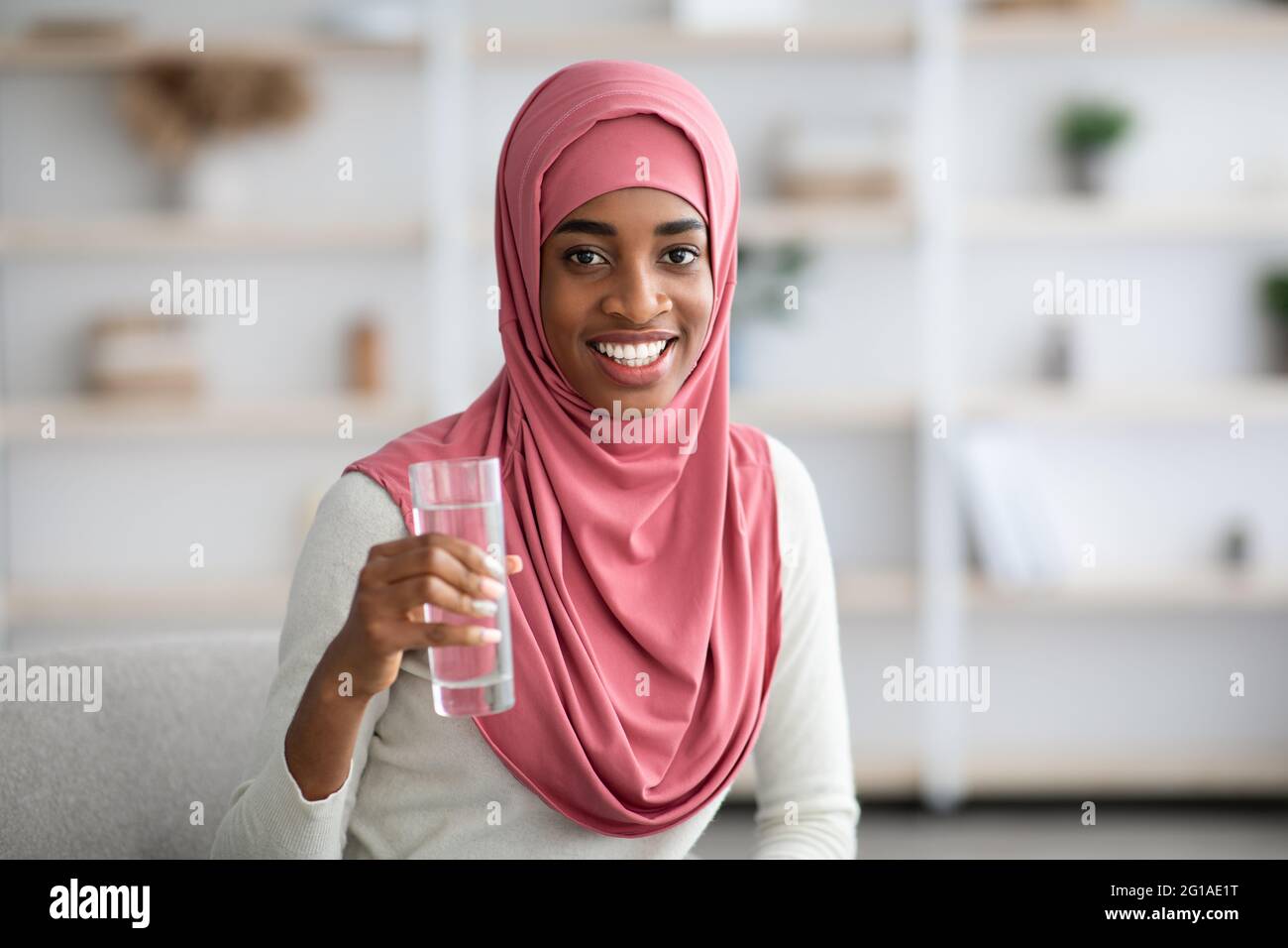 Smiling Black Muslim Lady In Hijab Drinking Water From Glass At Home ...