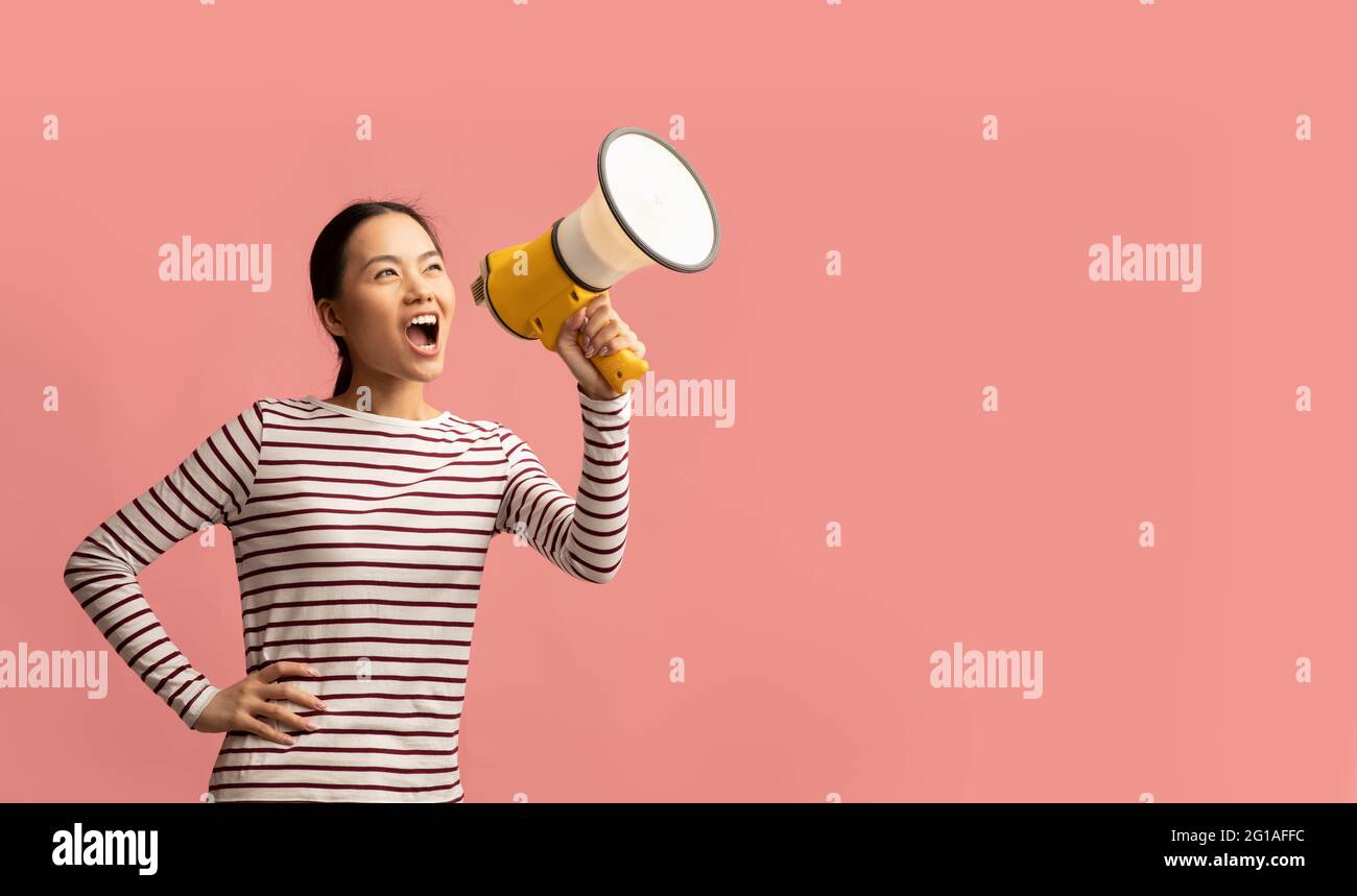 Asian Female With Megaphone In Hands Making Announcement, Shouting At Copy Space Stock Photo