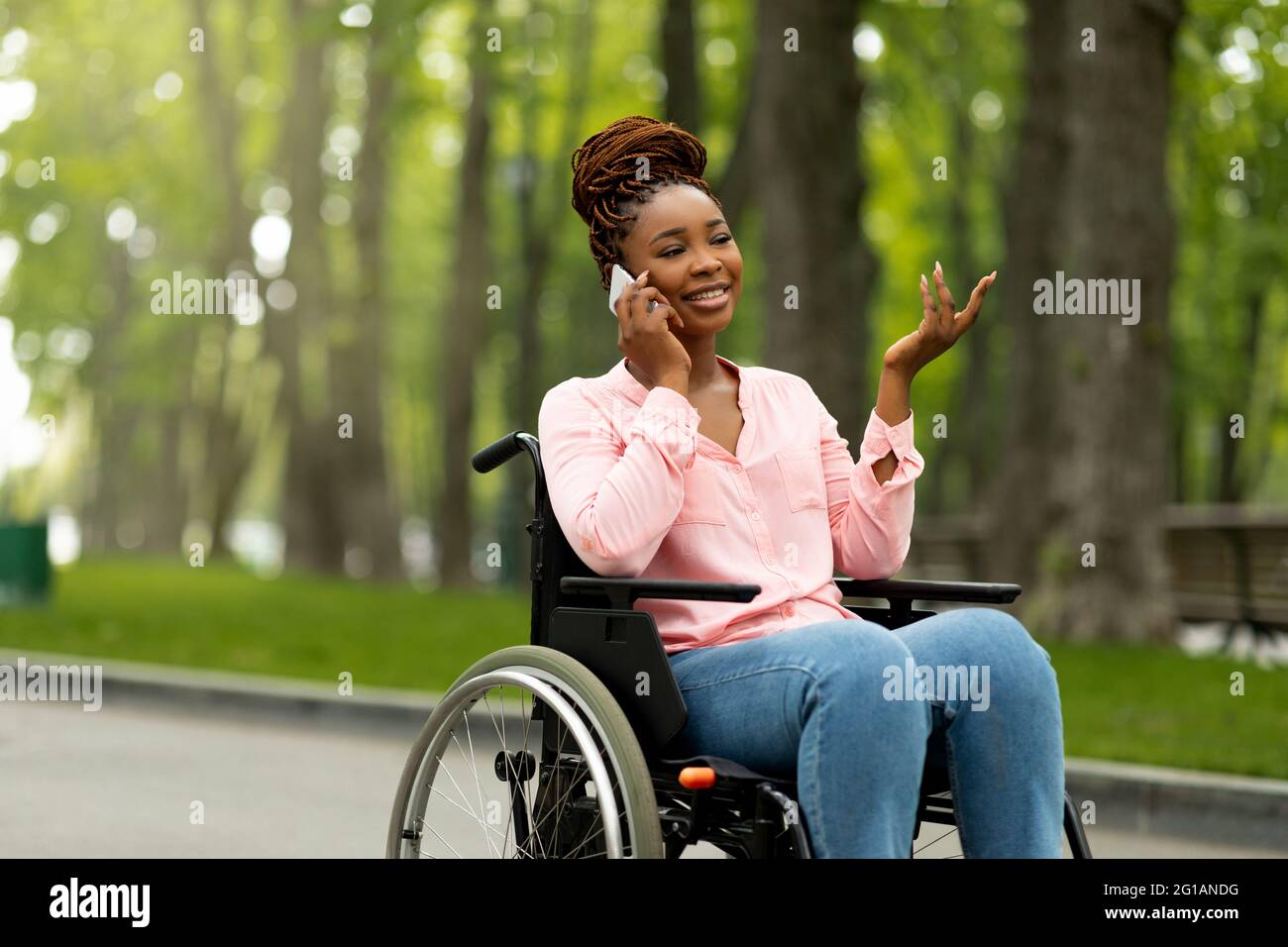 Joyful black lady in wheelchair having phone conversation with friend
