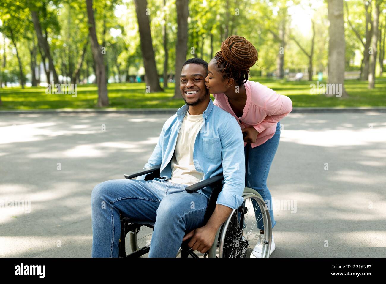 Affectionate black woman kissing her disabled husband in wheelchair