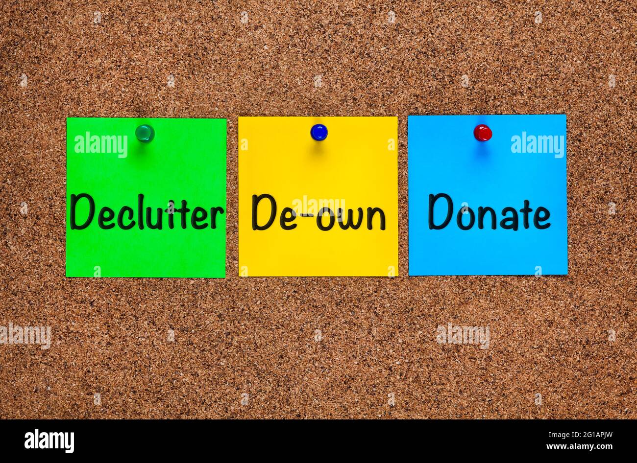 Three colored notes on corkboard with words Declutter, De-own, Donate. Close-up Stock Photo