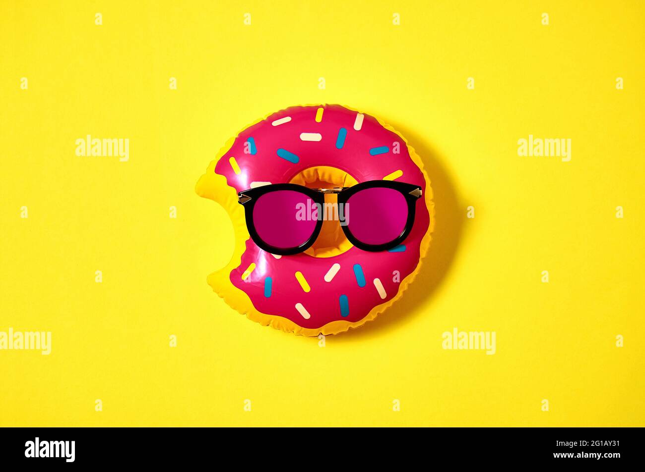 Inflatable donut in pink sunglasses on yellow background. Creative minimal concept. Top view Flat lay Stock Photo