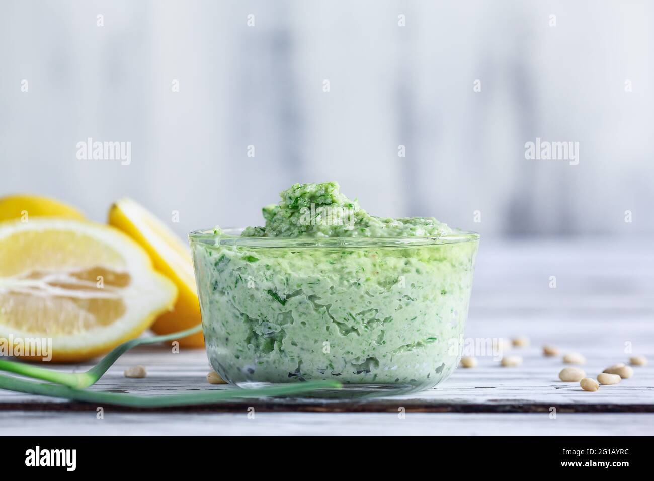 Garlic Scape Pesto with fresh homegrown ingredients of scapes, lemons, pine nuts and parmesan cheese over a white rustic wood table. Selective focus w Stock Photo