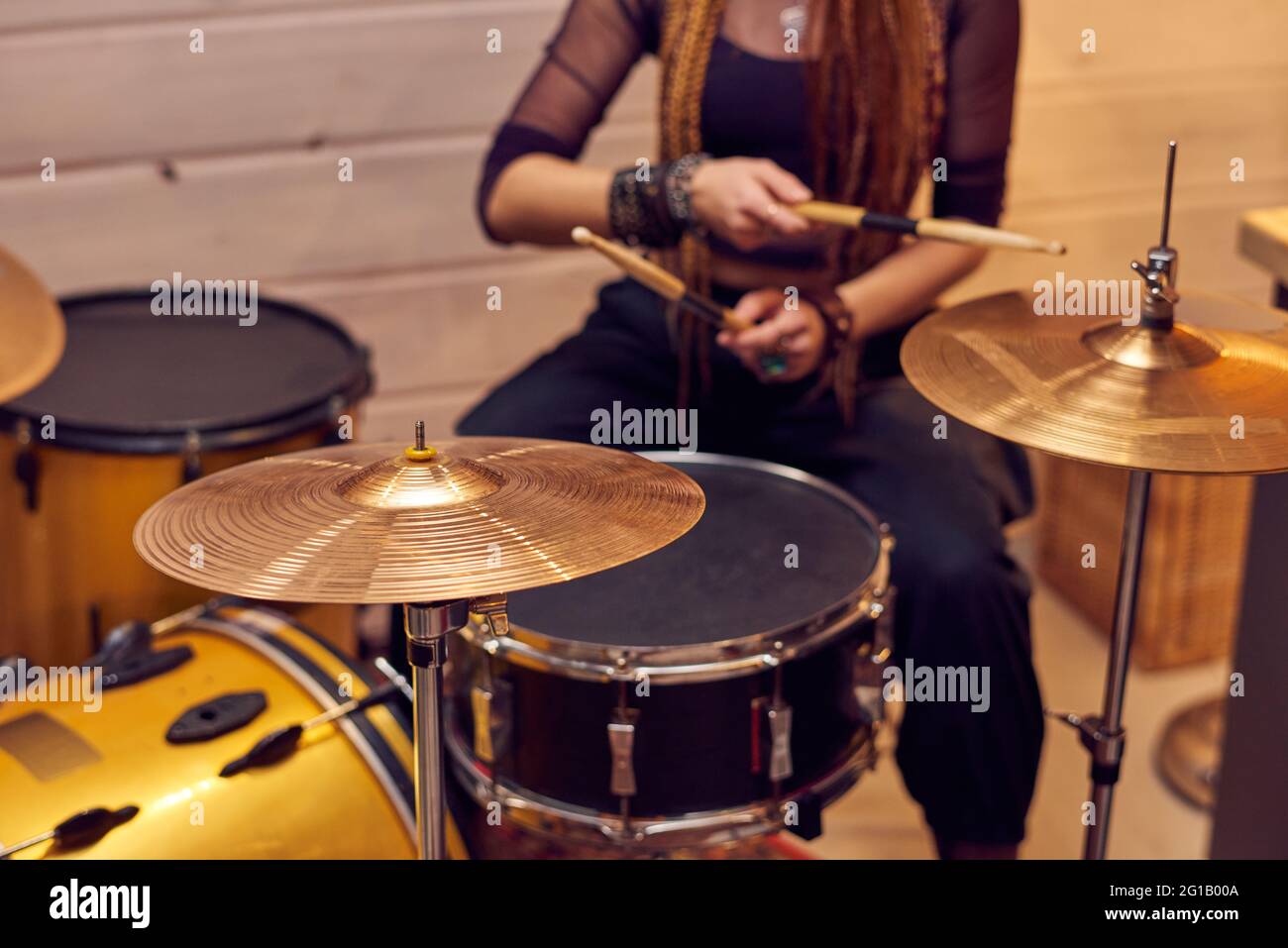 Drum set and young female with drumsticks sitting near by Stock Photo