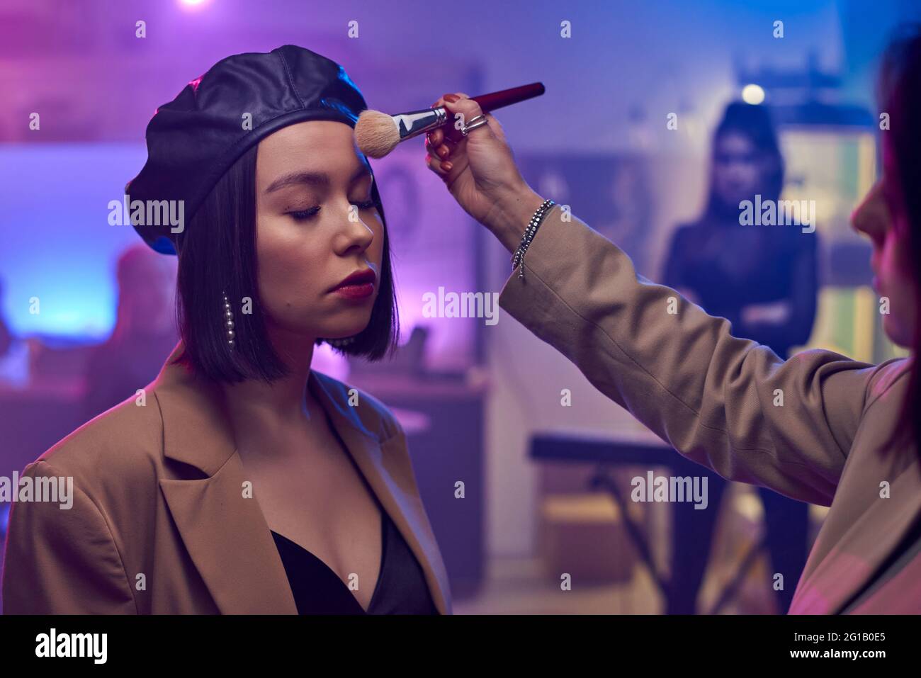 Make-up artist applying powder on face of young female musician before shooting of performance Stock Photo