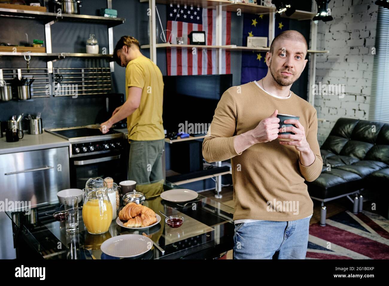 Young man with mug standing by table against another guy Stock Photo