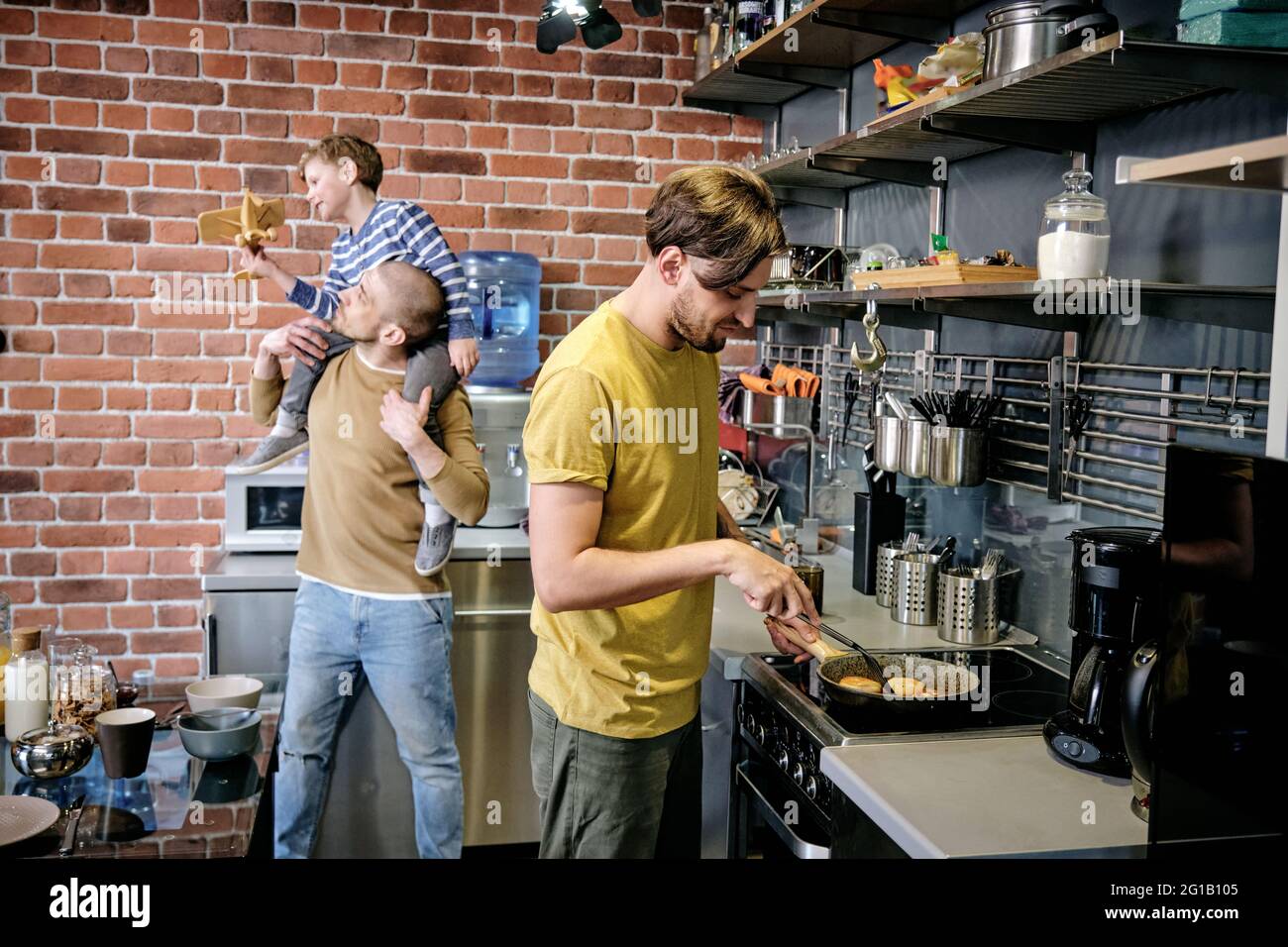 One of two gay men cooking by stove against his husband playing with boy Stock Photo