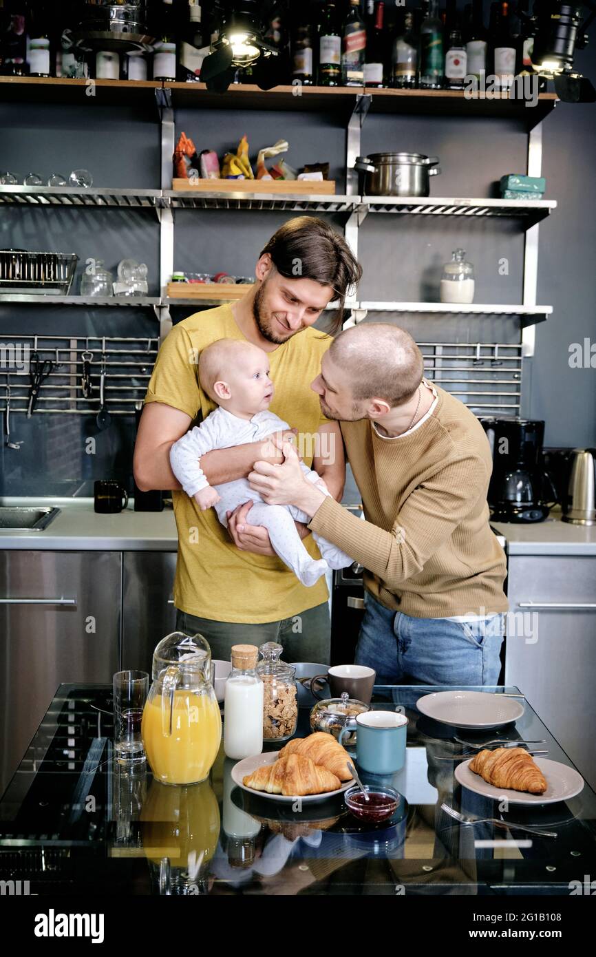 Two cheerful gay men playing with baby boy in the kitchen Stock Photo