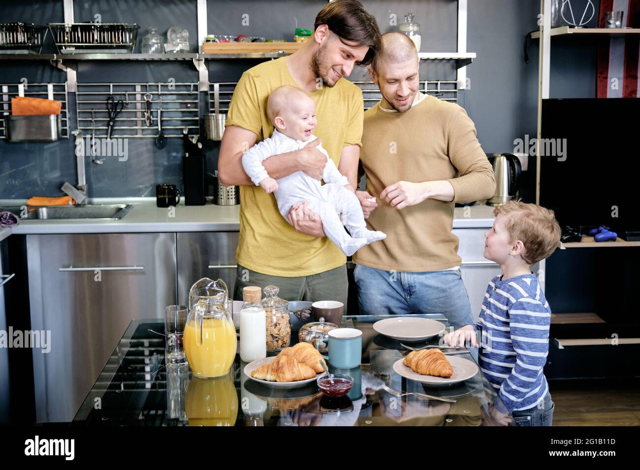Two young gay men playing with two boys by kitchen table Stock Photo
