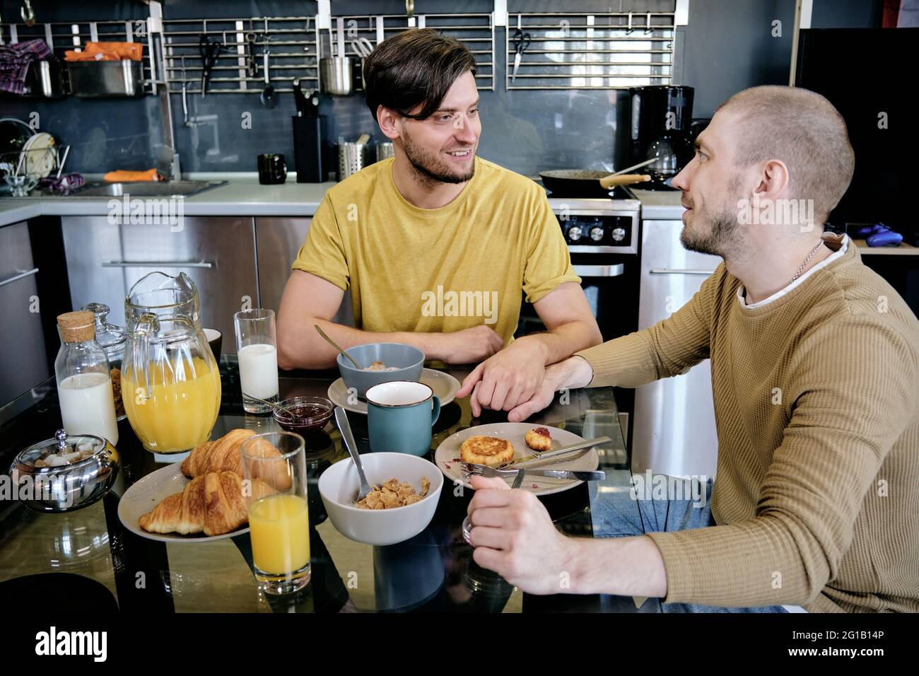 Two guys holding by hands during breakfast in the kitchen Stock Photo