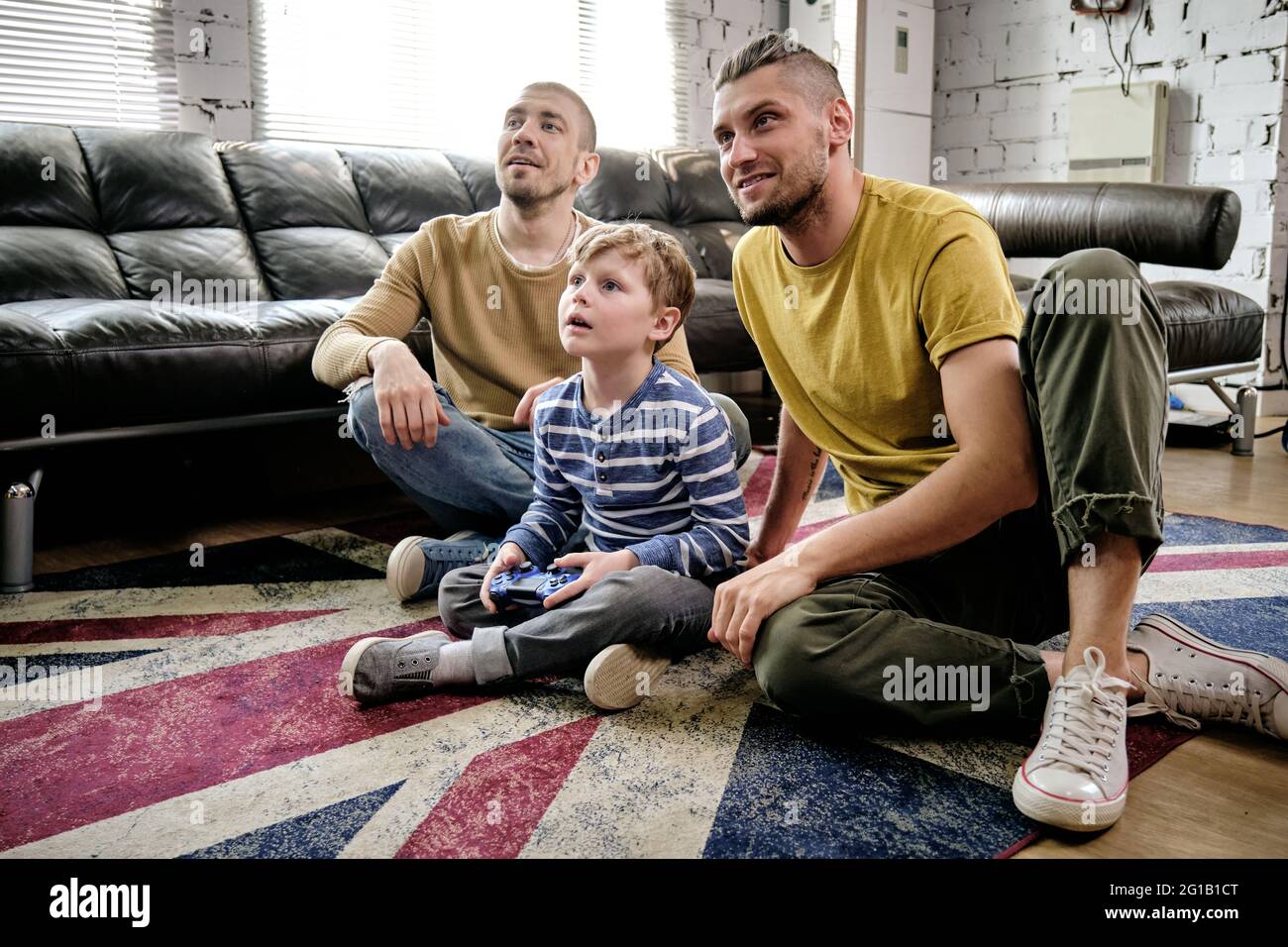 Cute boy and two guys watching television while sitting on the floor Stock Photo