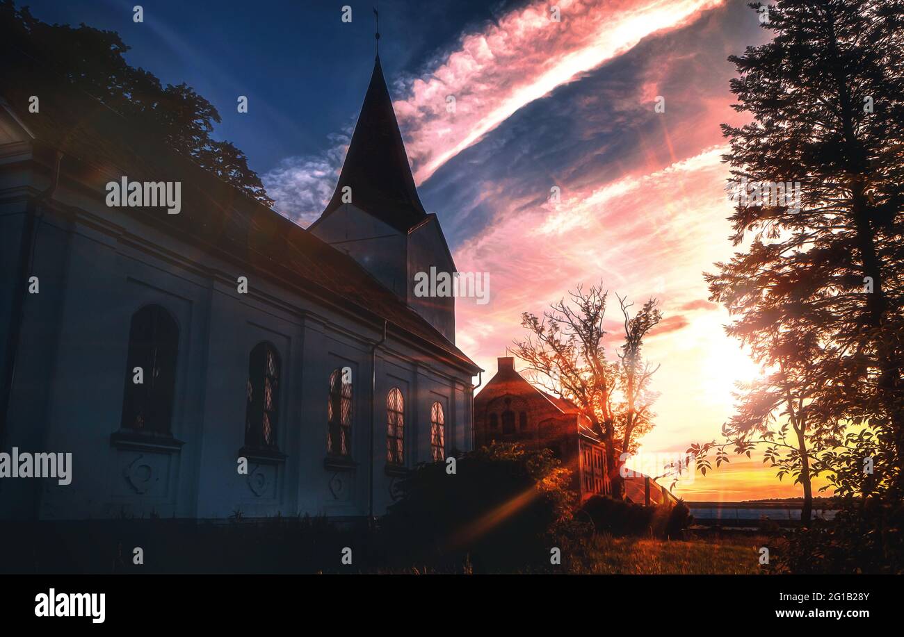 Kirche bei dramatischem Sonnenuntergang mit Sonnenstrahlen im Sommer in Polen. Kirchengebäude im Morgengrauen mit göttlichen Lichtstrahlen Stock Photo