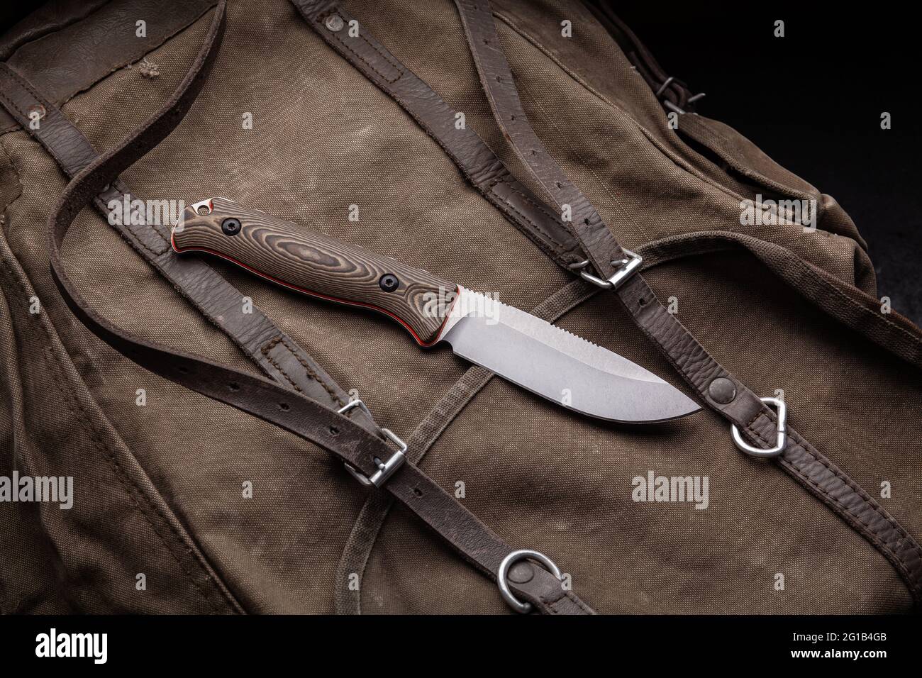 A hunting knife with a wooden handle on a khaki canvas backpack. Weapons for self-defense and survival. Stock Photo
