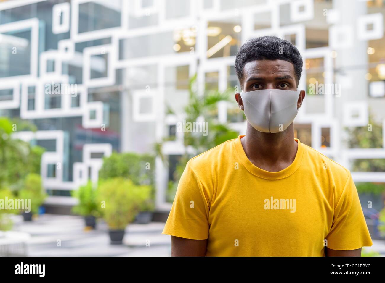 Portrait of handsome black African man wearing yellow t-shirt outdoors in city in Bangkok, Thailand Stock Photo