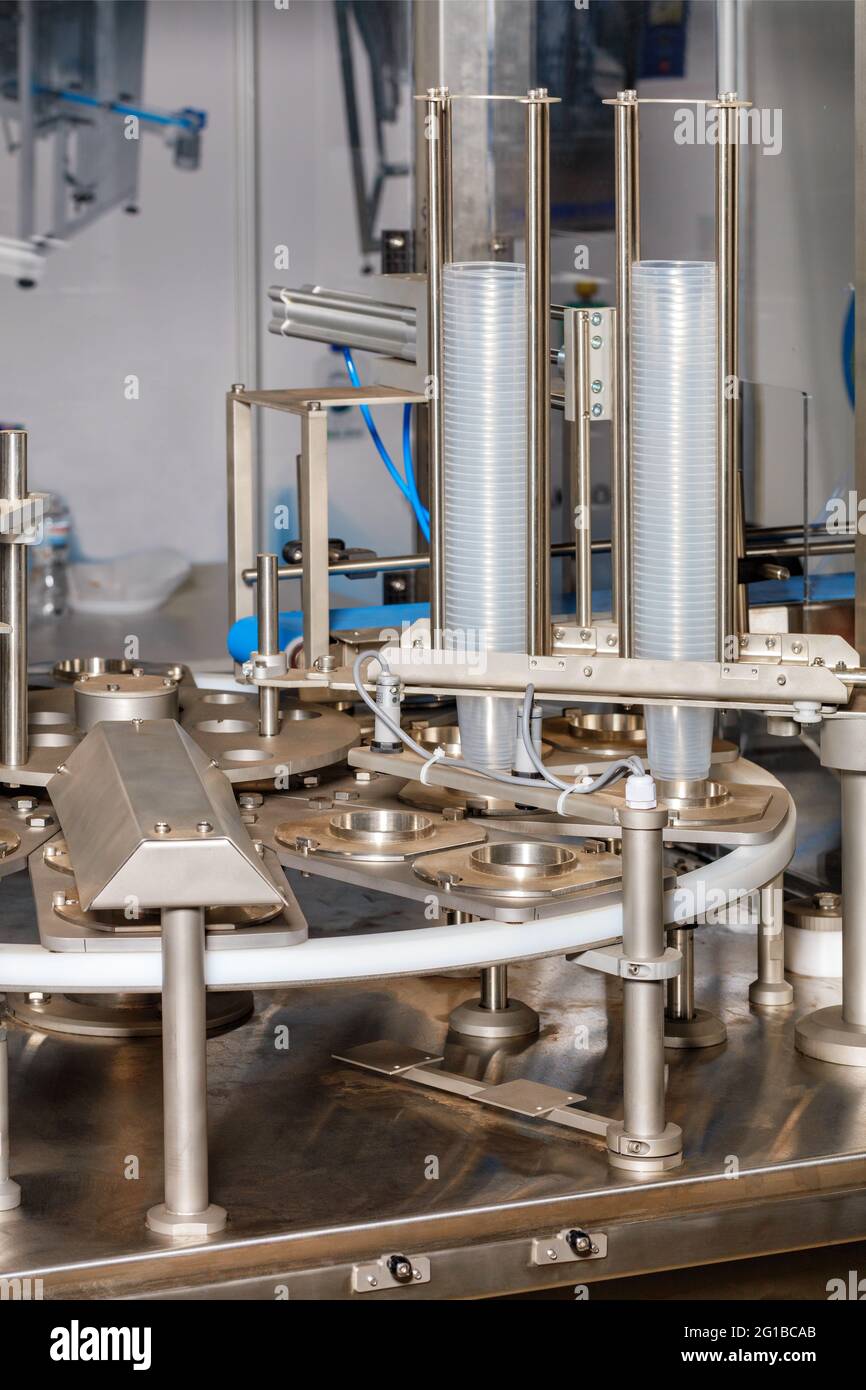 Fragment of a food industry production line for filling and packaging liquid products in plastic cups. Vertical image, close-up, copy space. Stock Photo