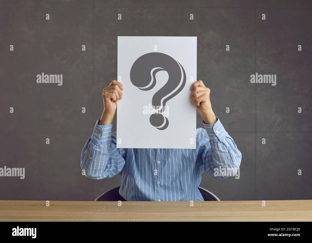 Unknown business man hiding his face behind a sheet of paper with a question mark Stock Photo