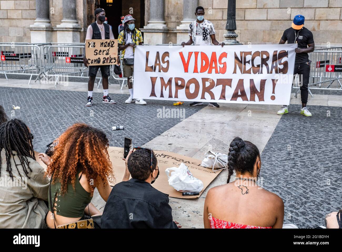 Barcelona, Spain. 06th June, 2021. Protesters seen sitting on the ground facing a banner saying Black lives matter during the demonstration. Summoned by Black Community Resists, a group of people have gathered in Plaza de Sant Jaume to commemorate the year of the murderer of the American citizen, George Floyd and denounce systemic and structural racism. Credit: SOPA Images Limited/Alamy Live News Stock Photo