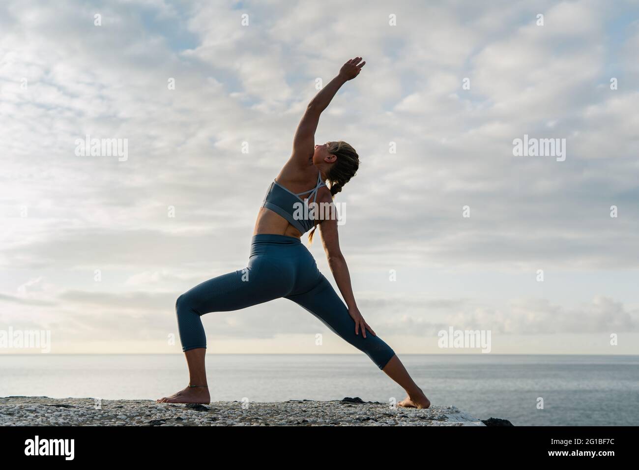 Back view of female in sportswear practicing yoga with raised arm on ocean  shore under cloudy sky Stock Photo - Alamy