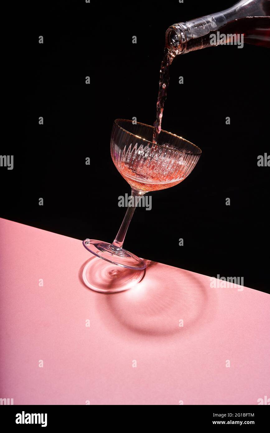 Anonymous person pouring rose sparkling wine into elegant coupe glass against two colored background Stock Photo