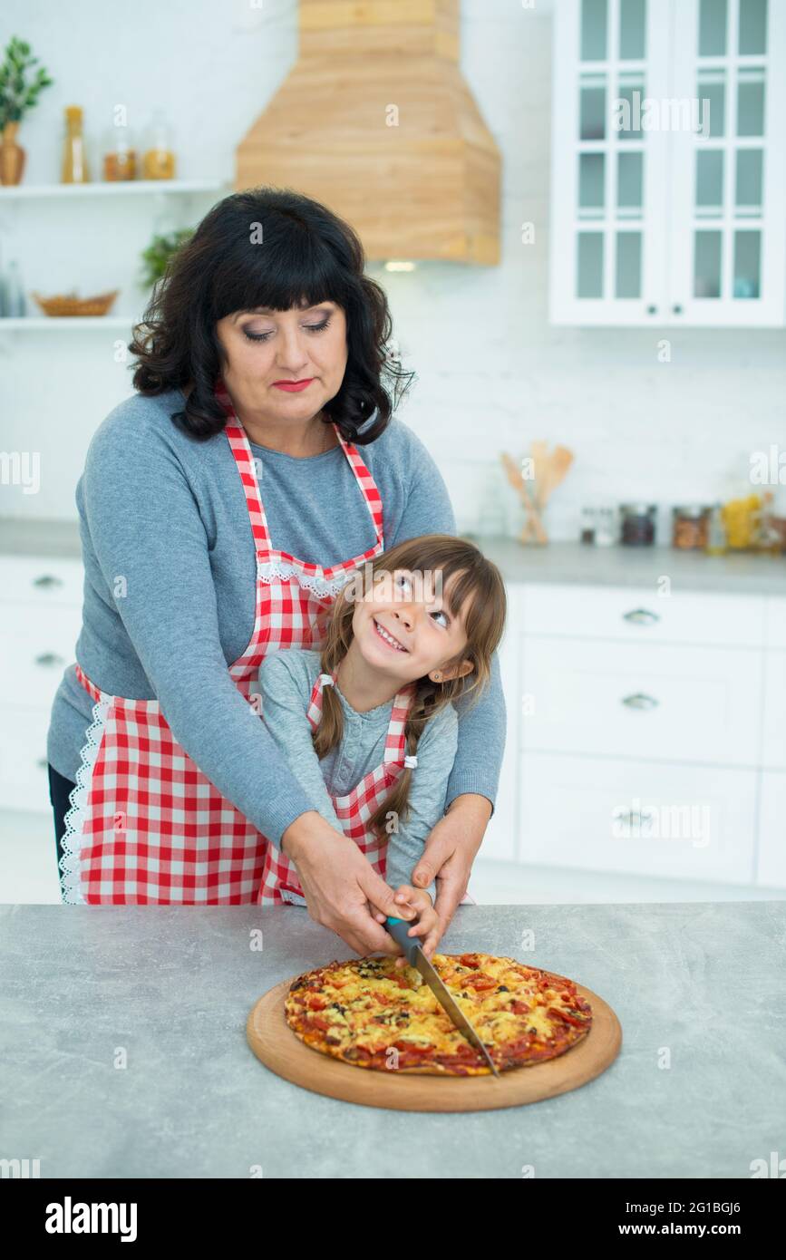 Grandmother and granddaughter cut the finished pizza with a knife