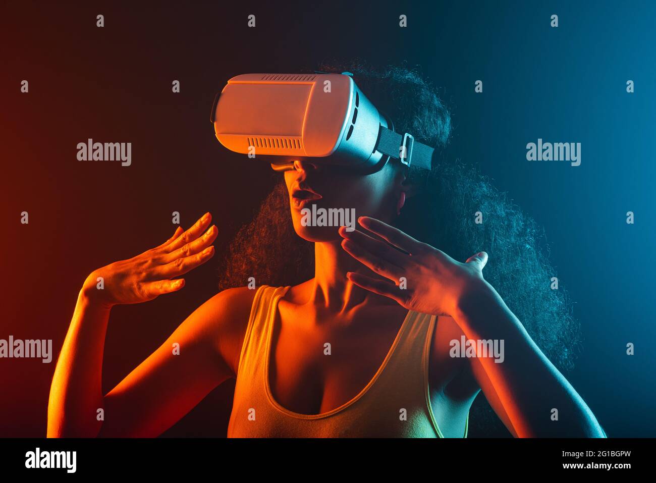 Anonymous astonished ethnic female with open mouth exploring virtual reality in headset on black background Stock Photo