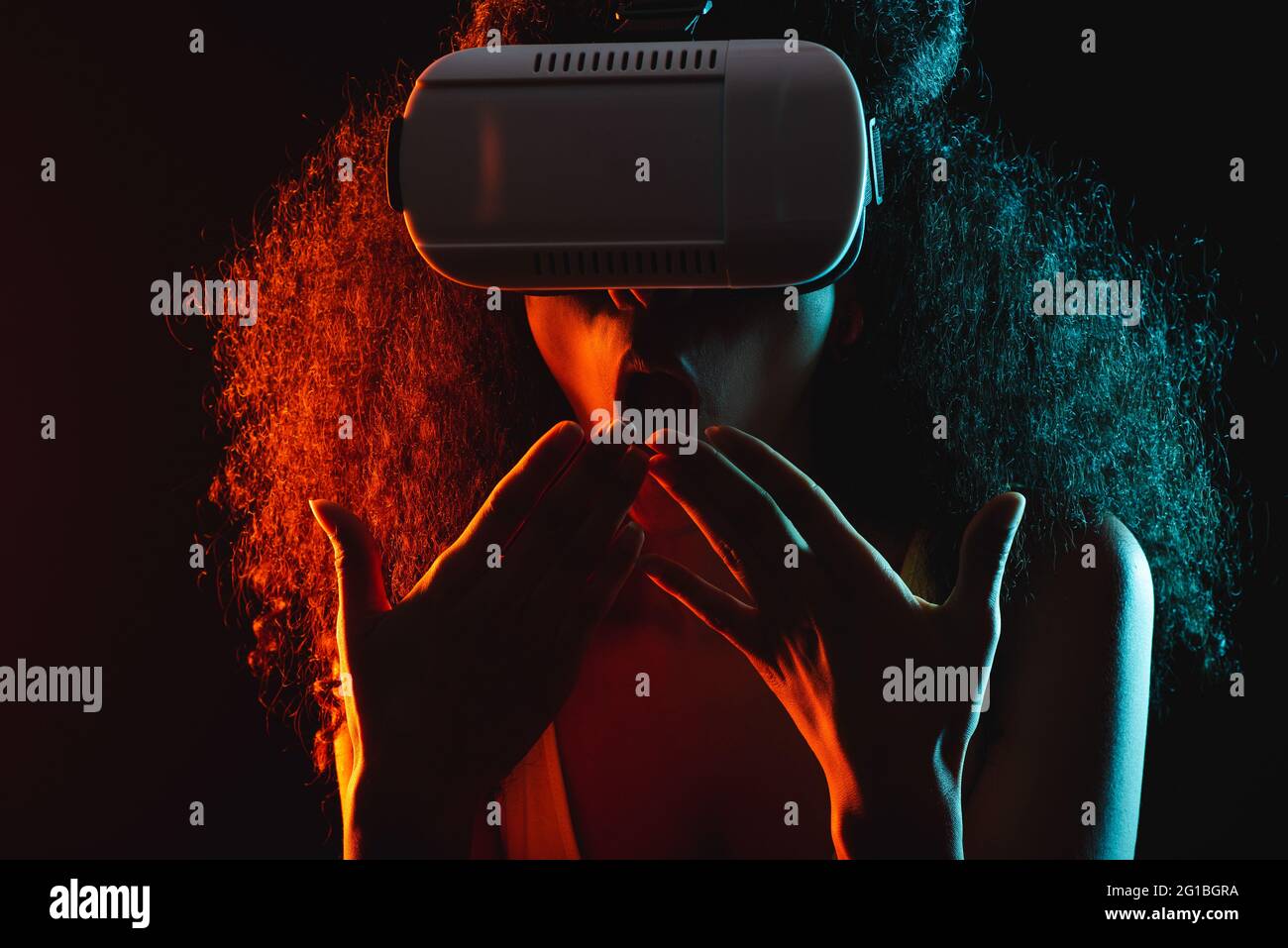Anonymous astonished ethnic female with open mouth exploring virtual reality in headset on black background Stock Photo