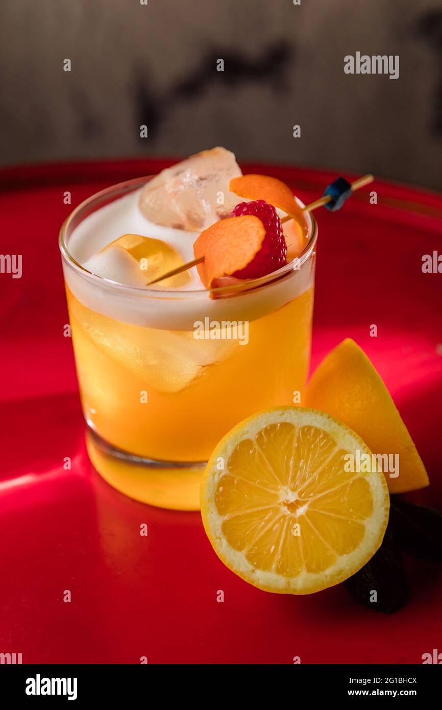Crystal glass of Amaretto Sour cocktail garnished with orange zest and  raspberry served with halved lemon Stock Photo - Alamy