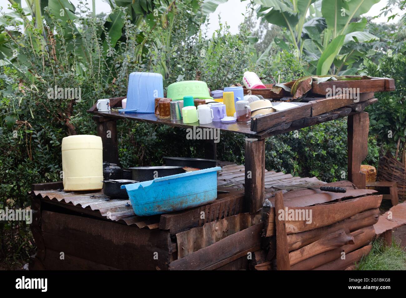 Cups, mugs, plates and bowls made of plastic and ceramic stand on a leaning wooden table with a wooden cabinet underneath in the open air Stock Photo