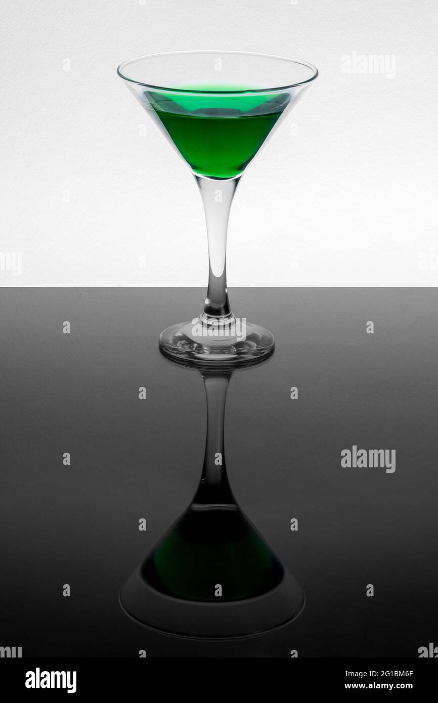 Green liquid in martini glass on white background. Mirror reflection on a black table Stock Photo