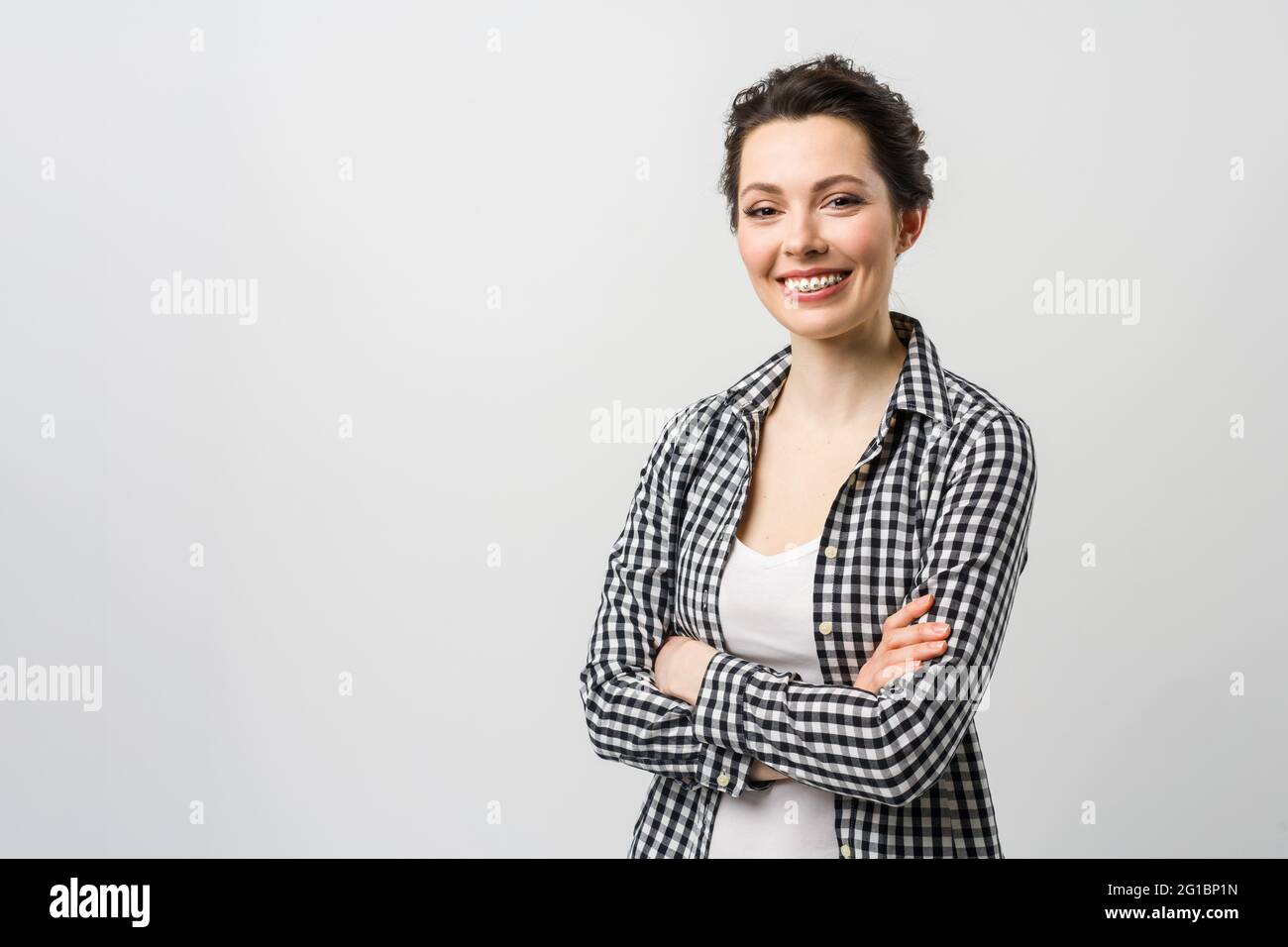 Business portrait of a young woman. A charming brunette looks at the camera, crossing her arms over her chest. Stock Photo