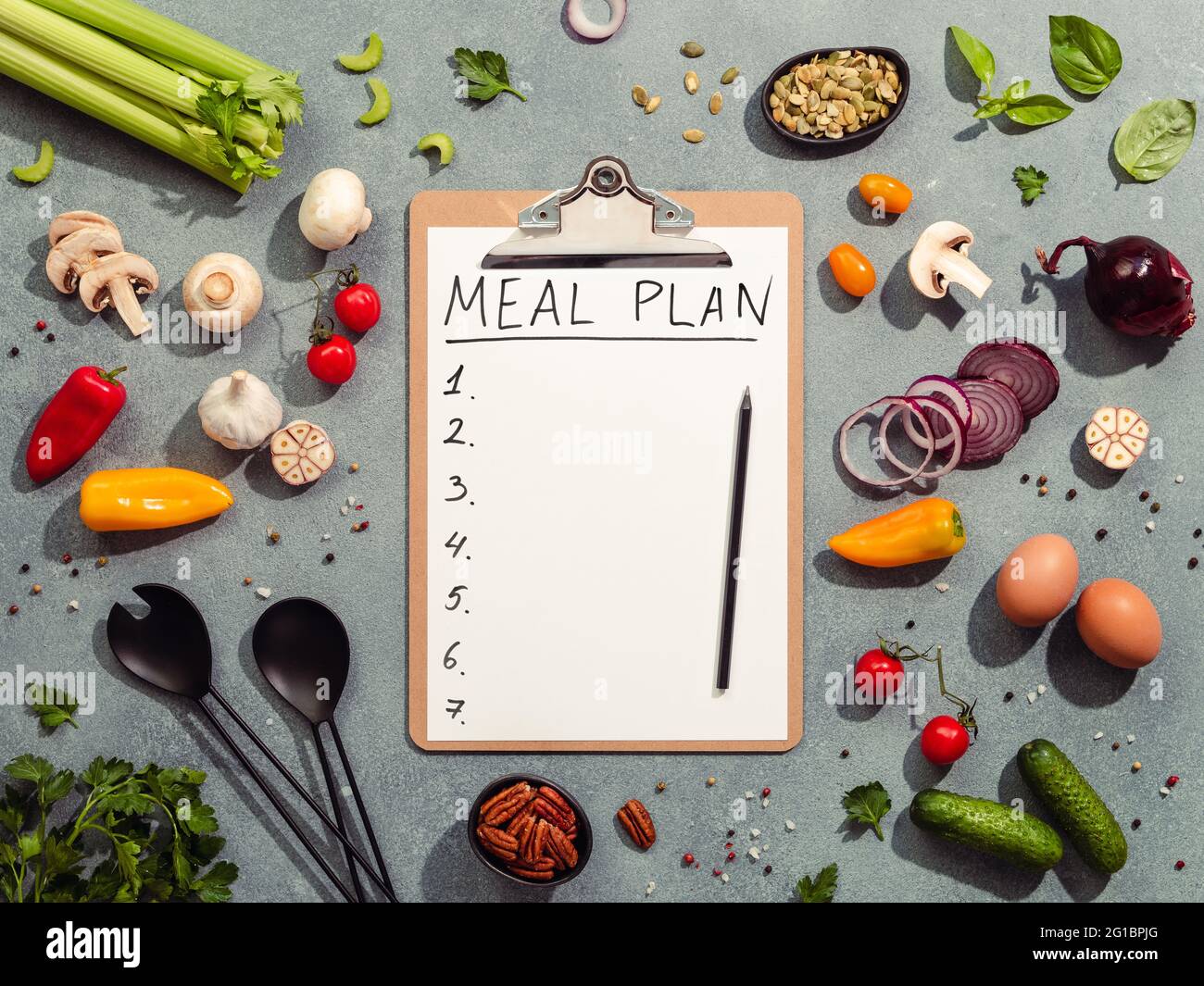 Meal plan concept. Food ingredients, salad serving utensils and clipboard with letters MEAL PLAN and seven numbers. Gray background. Diet menu concept. Top view, flat lay Stock Photo
