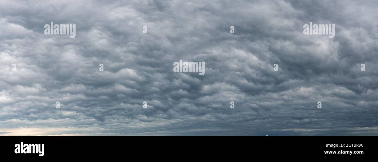 Low gray stratocumulus clouds covered the whole sky. Dark overcast sky panorama. Wide image of scenic rainy clouds. Dramatic sky before the rain. Stock Photo