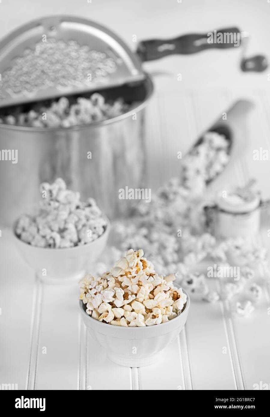Old fashion popcorn maker, in messy popcorn scene, with white bowls full of popcorns, vintage ambience, wooden scoop. Stock Photo